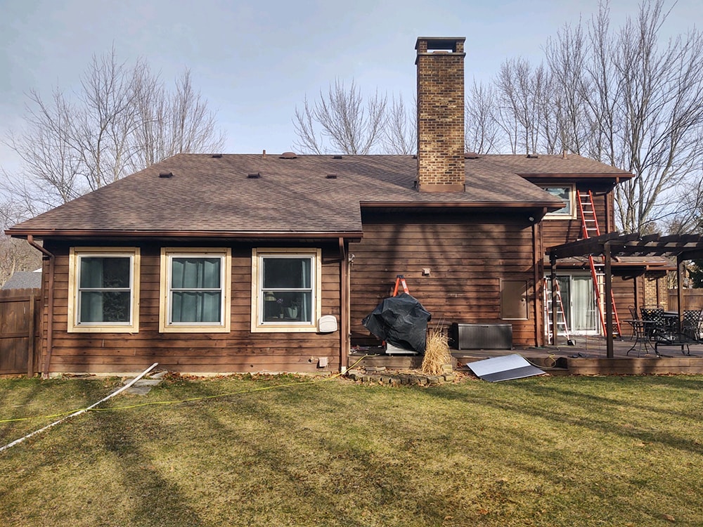 Siding job with brick — before: side rear view of home with original dark wood siding and new windows staged, Findlay, Ohio