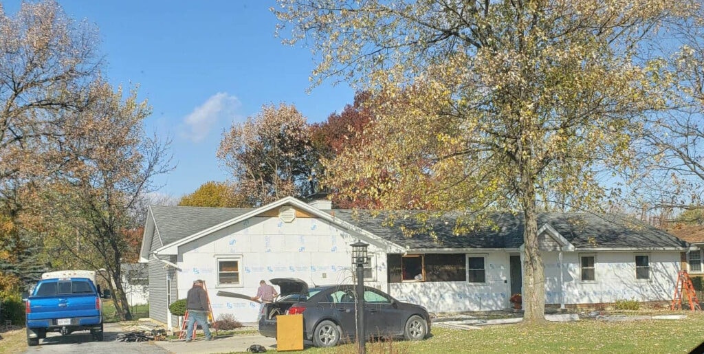 Stone siding Findlay — during: exterior wide view of home stripped to Typar house wrap with crew and blue truck in driveway, fall foliage, Findlay, Ohio
