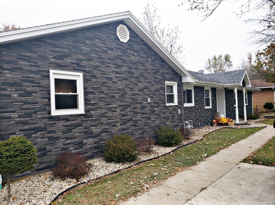 Stone siding Findlay — after: completed exterior with full dark gray stacked stone siding, new white-trimmed windows, white fascia, and fall landscaping, Findlay, Ohio