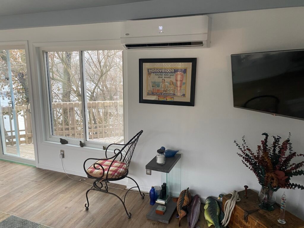 Sunroom transformation Fostoria — after: interior corner with mini-split HVAC unit, large sliding window overlooking snowy deck and frozen water, LVP flooring, and vintage decor, Fostoria, Ohio