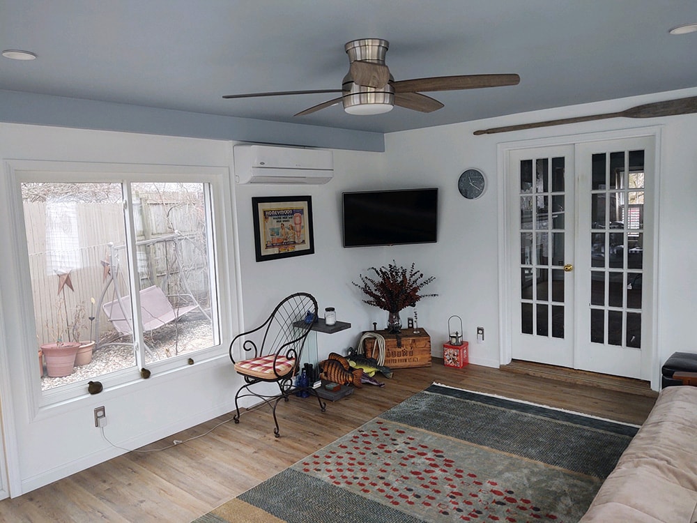 Sunroom transformation Fostoria — after: interior showing mini-split HVAC, mounted TV, French doors to home, ceiling fan, LVP flooring, and sliding window with backyard view, Fostoria, Ohio