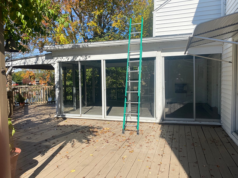 Sunroom transformation Fostoria — before: close-up of original aluminum sunroom exterior with sliding glass panels and green ladder, Fostoria, Ohio