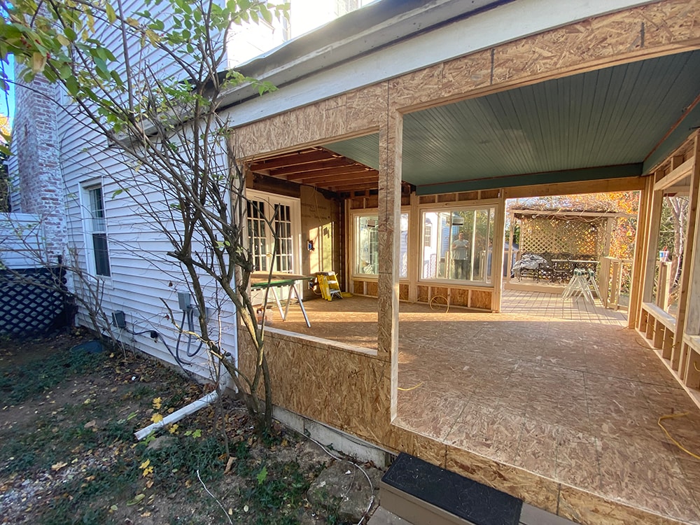 Sunroom transformation Fostoria — framing stage: side view of new OSB sheathed addition with open wall framing, existing windows, and crew member visible inside, Fostoria, Ohio
