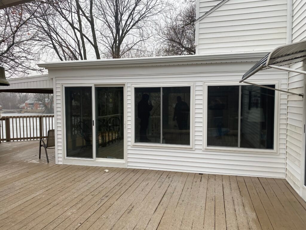 Sunroom transformation Fostoria — after: exterior close-up of completed addition with new white vinyl siding, large sliding glass door, and picture window on wet winter day, Fostoria, Ohio