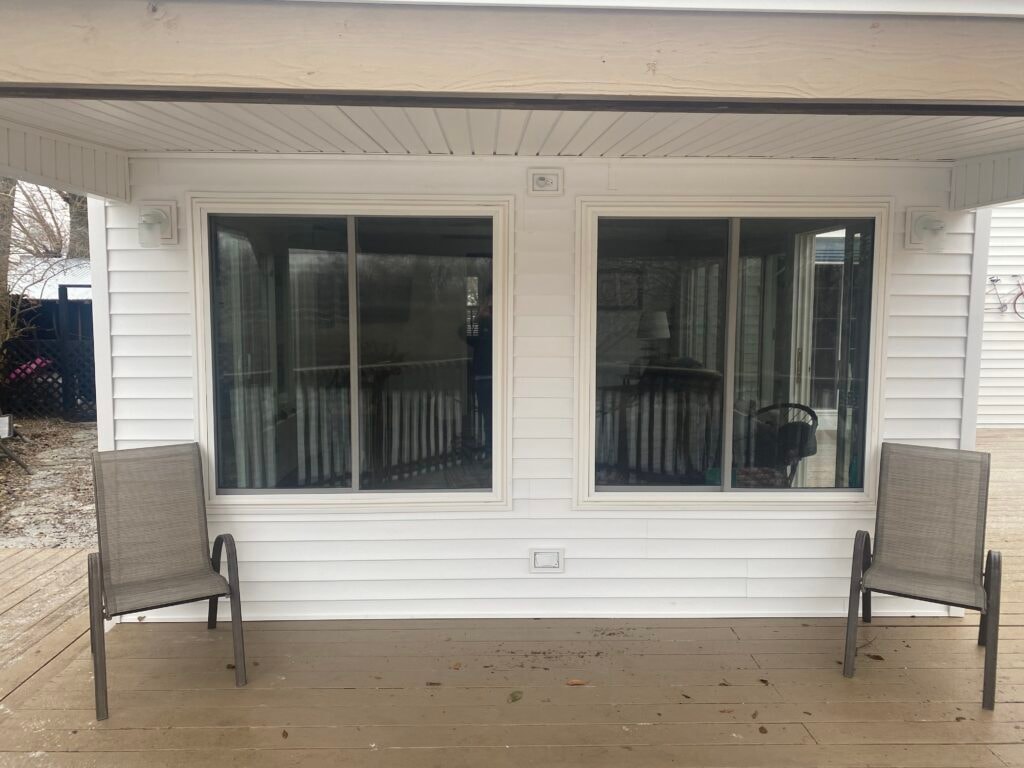 Sunroom transformation Fostoria — after: exterior other side of completed addition with two new sliding windows, white vinyl siding, and two patio chairs on deck, Fostoria, Ohio