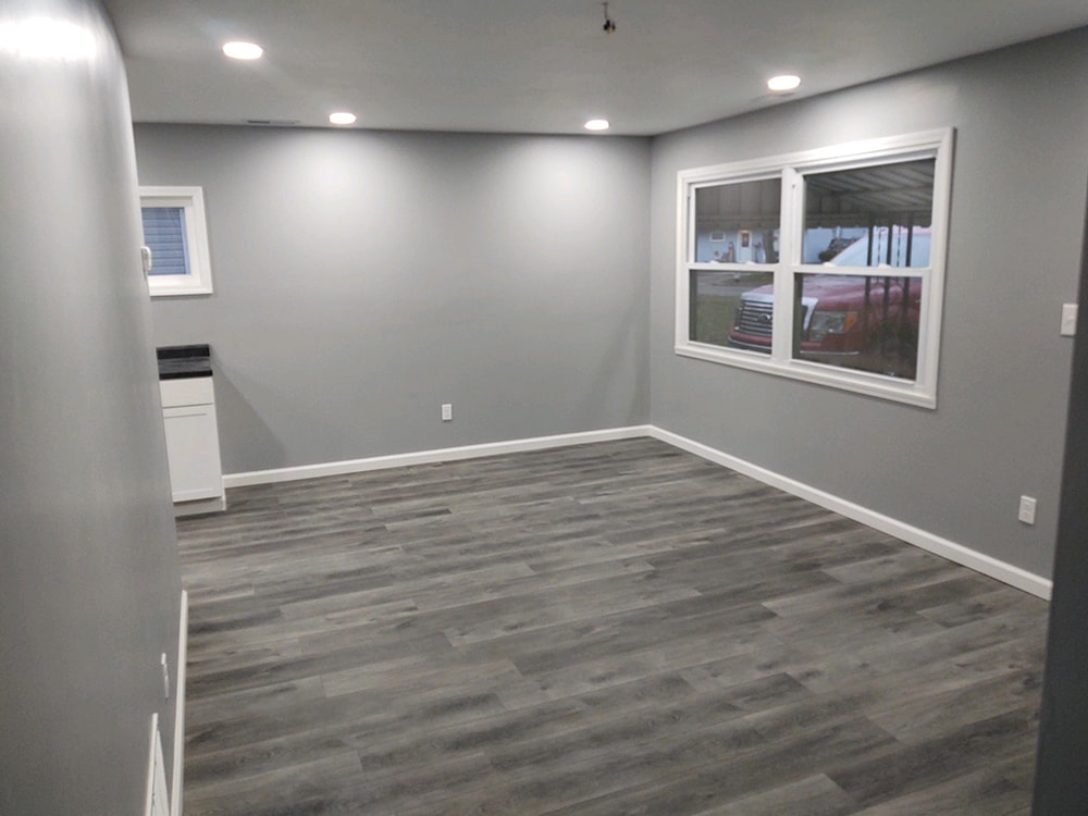 Whole house remodel after — living room with gray LVP flooring, recessed lighting, fresh gray paint, and new windows, Fostoria, Ohio