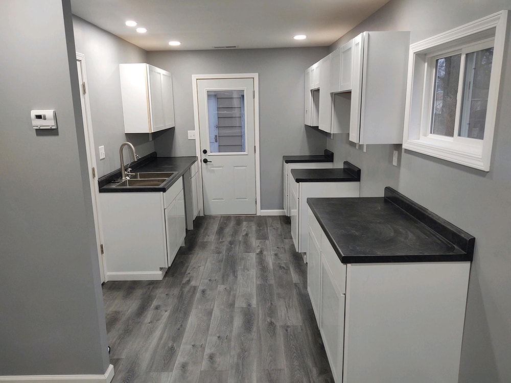 Whole house remodel after — kitchen with white shaker cabinets, black countertops, stainless sink, and gray LVP flooring, Fostoria, Ohio