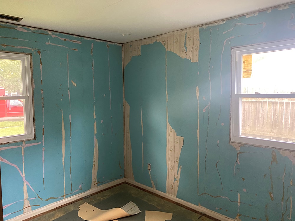 Whole house remodel before — bedroom with peeling teal paint, damaged walls, and bare subfloor, Fostoria, Ohio