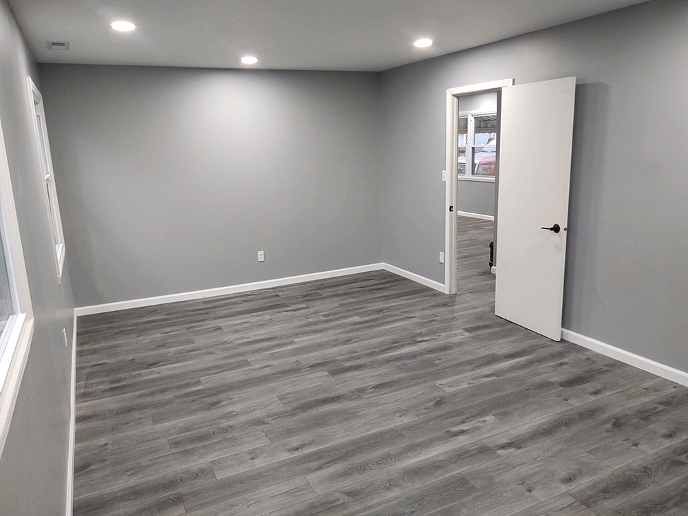 Whole house remodel after — bedroom with gray LVP flooring, fresh gray paint, recessed lighting, and new interior door, Fostoria, Ohio