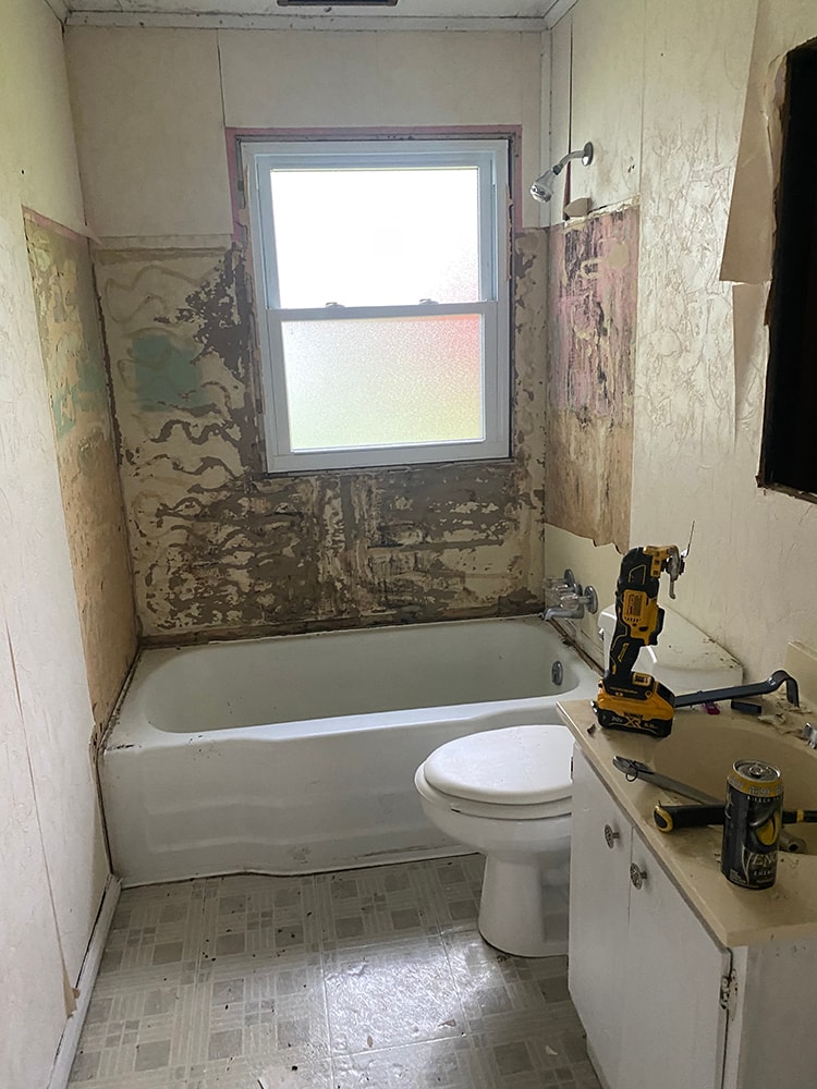 Whole house remodel before — bathroom gutted with deteriorated walls, old tub, toilet, and tile flooring mid-demolition, Fostoria, Ohio